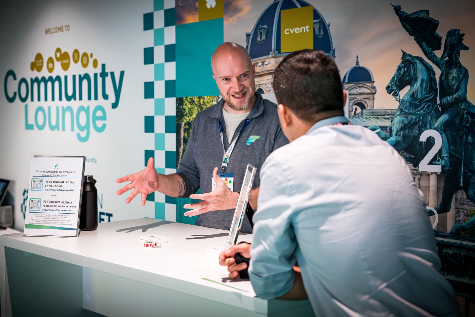 Seorang staf berbincang dengan pengunjung di meja Community Lounge pada konferensi komunitas Microsoft Fabric